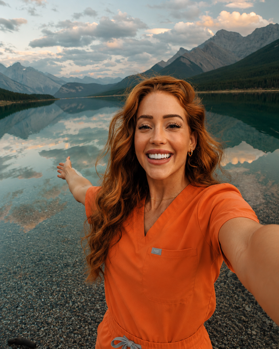 Smiling nurse in orange scrubs taking a selfie by a calm mountain lake